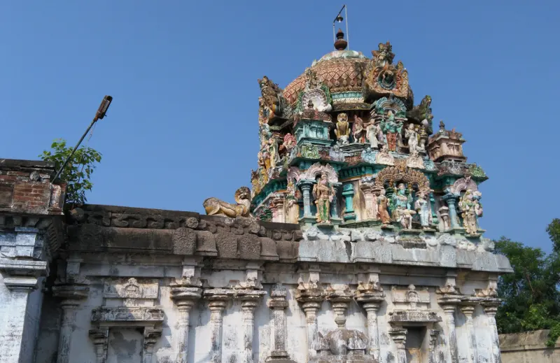 A colourful tower with many painted figures rising above a weathered white stone wall under a blue sky.