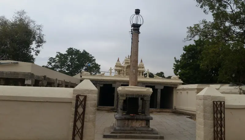 A tall stone pillar topped with a lamp cage on a stone base, with the entrance hall and its small tower behind.