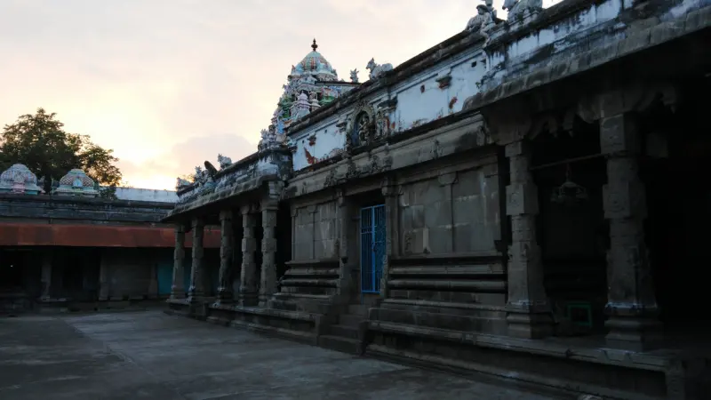Stone-pillared corridor with a small tower rising behind it under a dusky sky