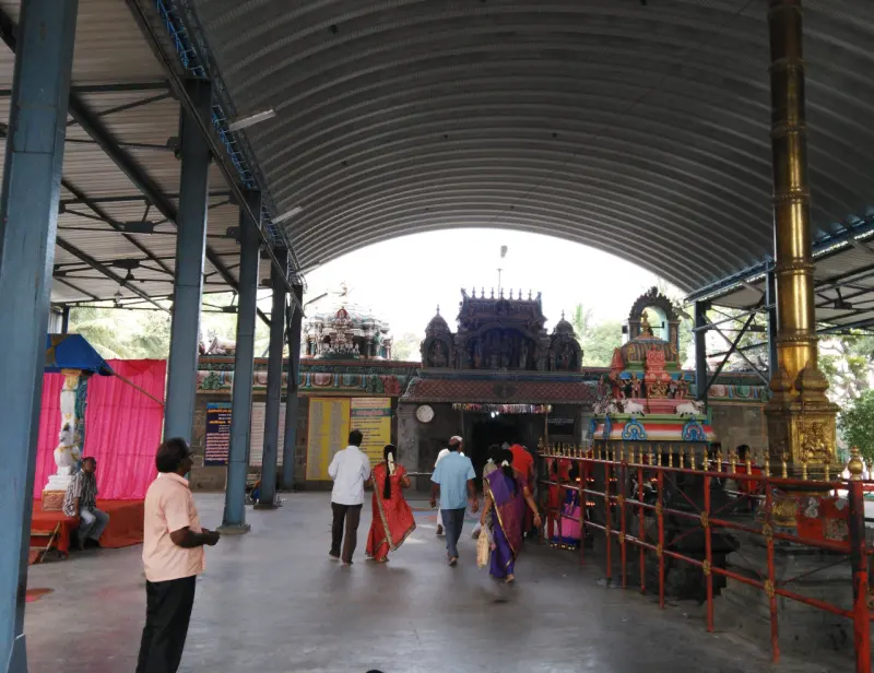 Devotees walking under a curved roof towards inner shrines, with a gold flagstaff at right.