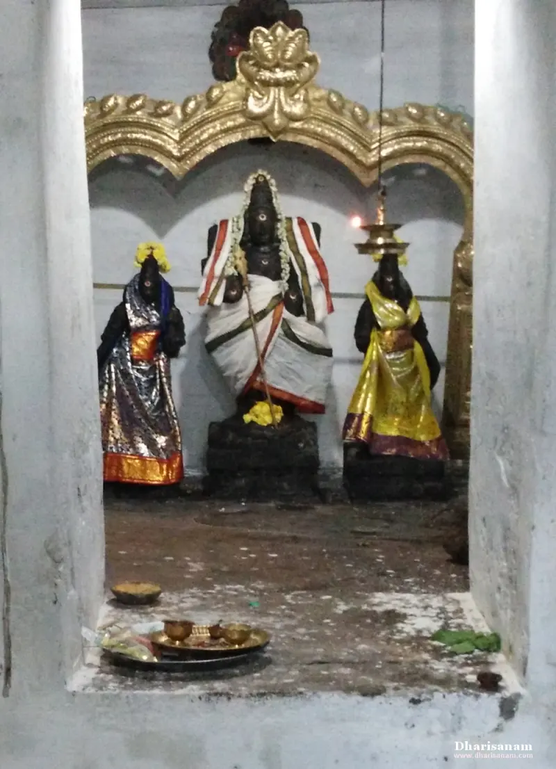 Three dark idols stand in a recess under a gilded arch, the central one in white cloth with a flower garland