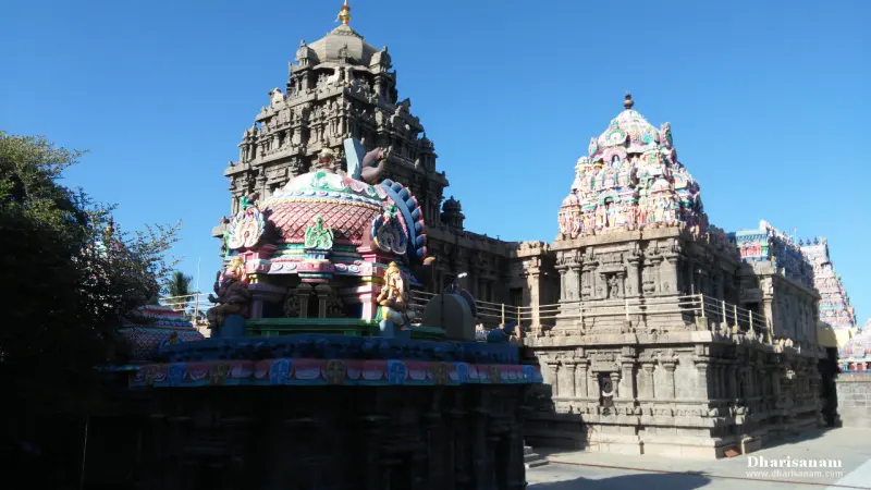 A dark granite tower and a painted tower on the sanctum, with a colourful shrine roof in front.