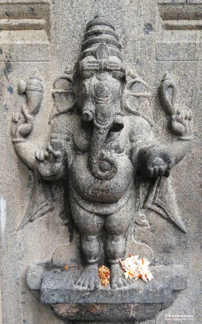 Four-armed Vinayakar carved in grey stone, with flowers at his feet