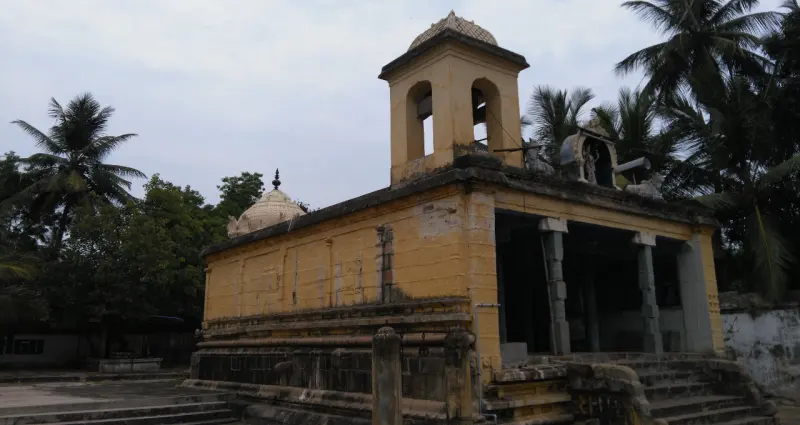 A yellow-walled porch with pillars and a small tower, steps leading up and coconut palms behind.