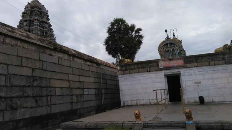 A small white shrine with guardian lions, a palm and the far tower