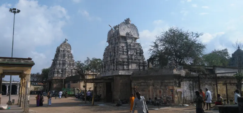 Two stone towers of different heights above a weathered wall, with people walking in the square below