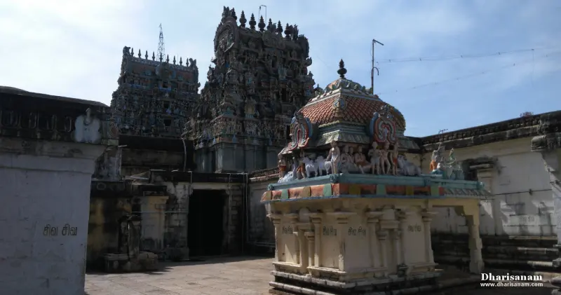 A small shrine with painted figures in a courtyard, two towers rising behind it