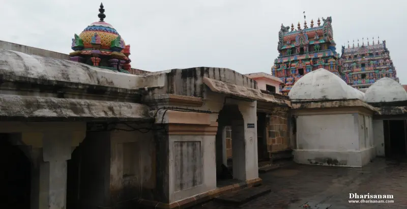Domed shrine roofs and a weathered stone wall, with two gopurams in the distance