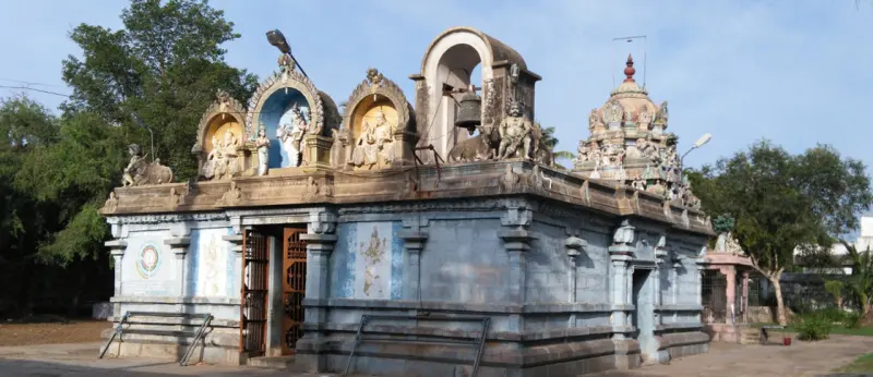 A blue-grey temple hall with figures above its door, and a painted tower rising behind on the right