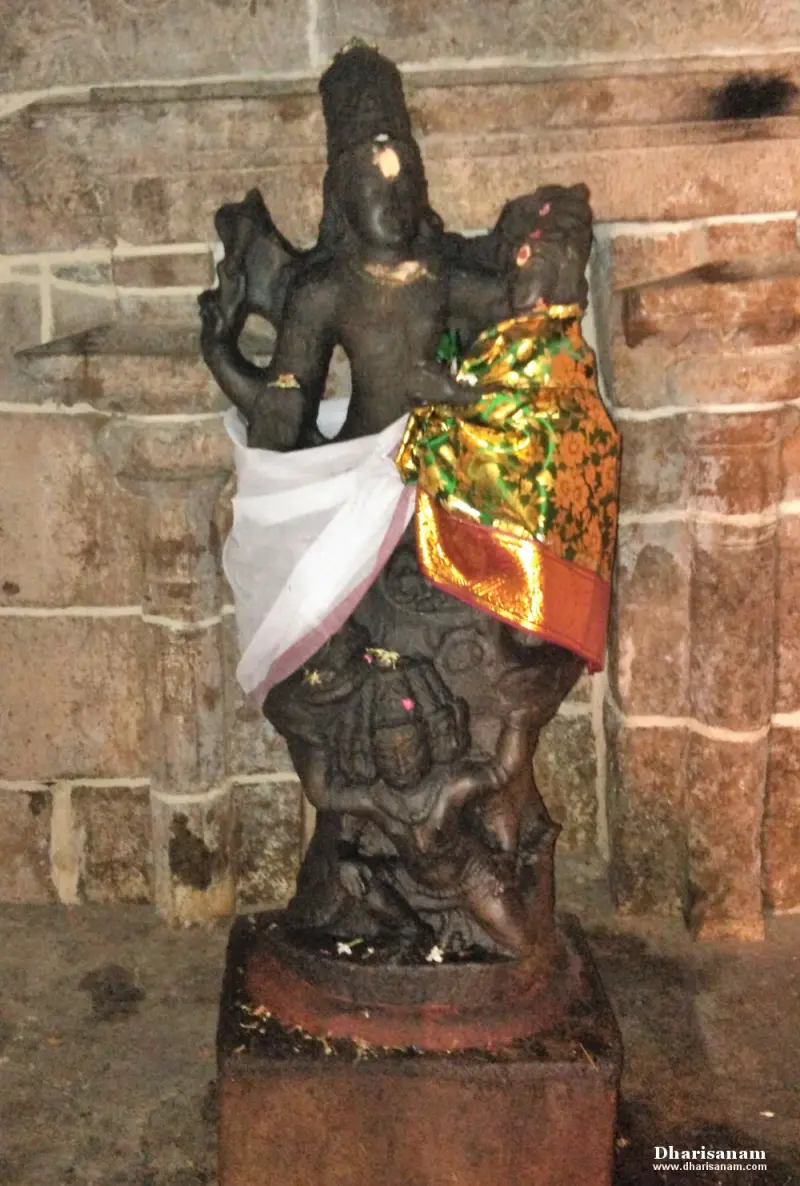 Dark stone idol draped in white and gold cloth, standing on a red base before a stone wall