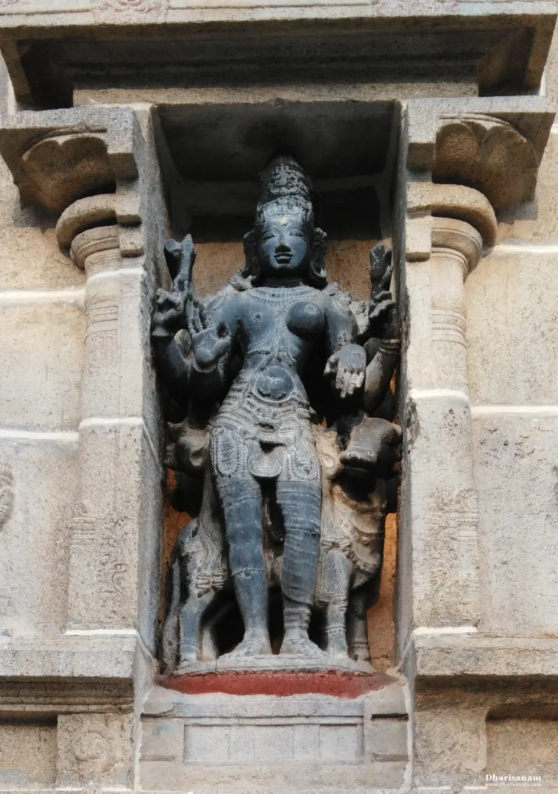 Grey stone sculpture of a many-armed goddess standing in a pillared niche on the temple wall