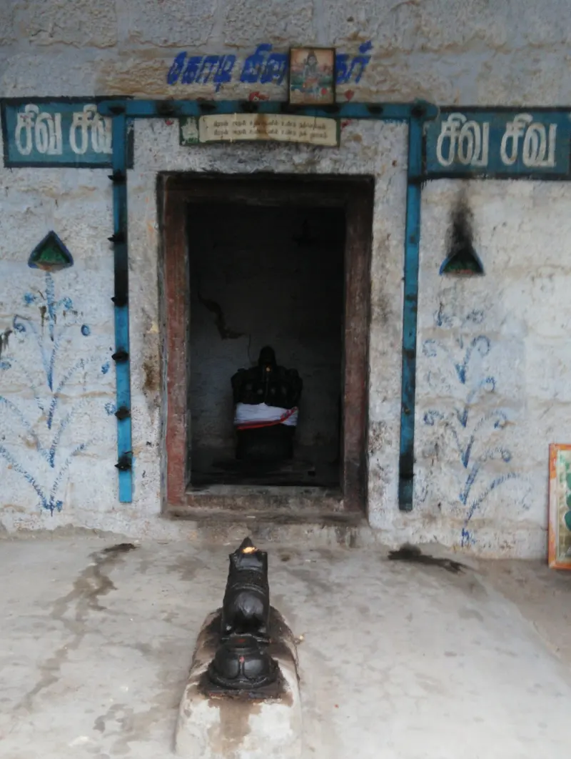 A whitewashed shrine doorway with Tamil signs, a dark idol inside and a small black bull in front