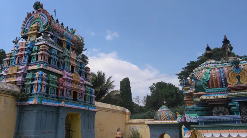 A tiered painted tower above the gateway at left and a richly painted shrine dome at right, against a blue sky