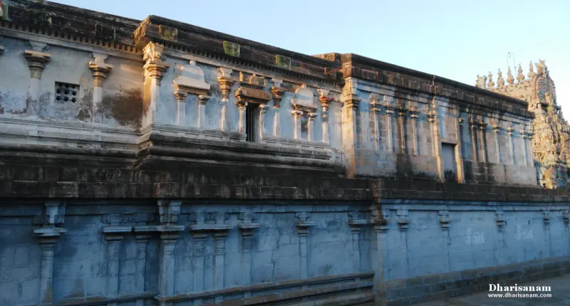 A long stone wall with rows of small pilasters and window frames, a gopuram partly visible at the far right