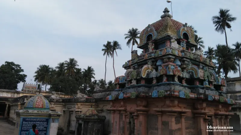 A coloured tiered tower above a red stone base, with small shrines and palm trees around it