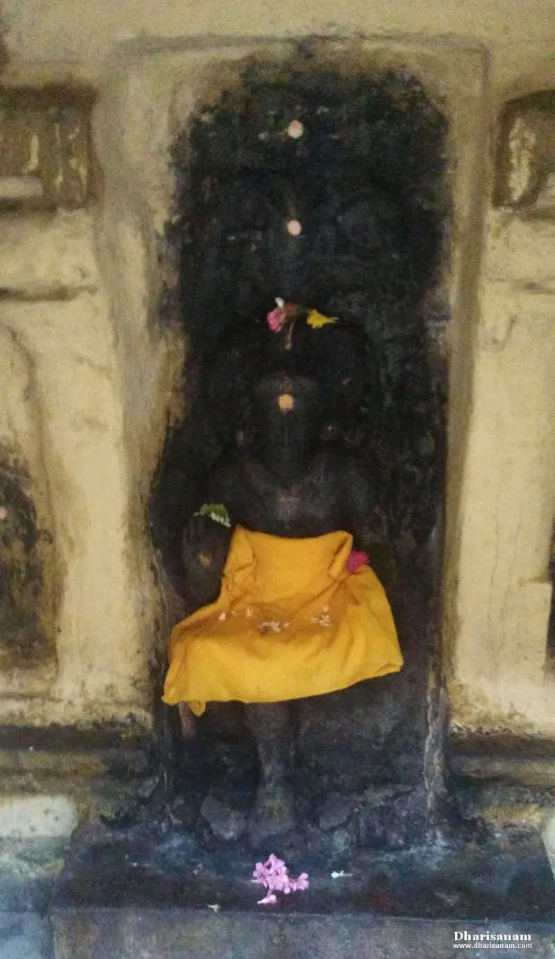 A dark stone image with a yellow cloth over its lap and flowers at its feet, in a niche.
