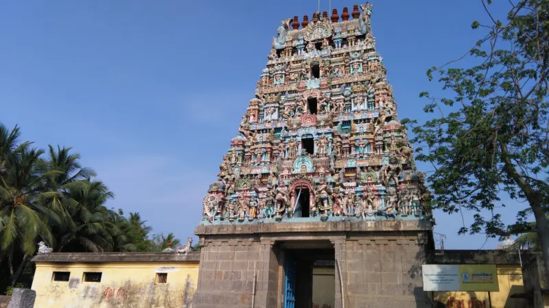 A tall tower covered in painted figures rises above a stone gateway against a blue sky