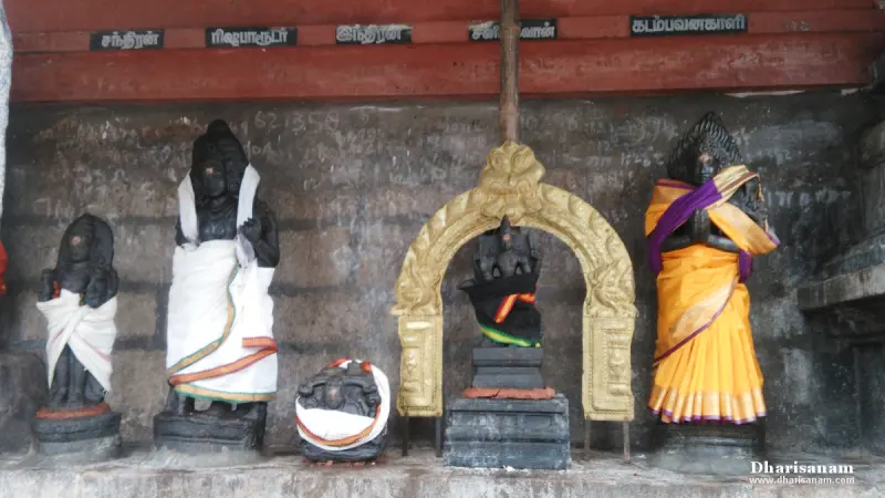 A row of black stone idols in cloth under name boards, with a small shrine in a gilded arch.