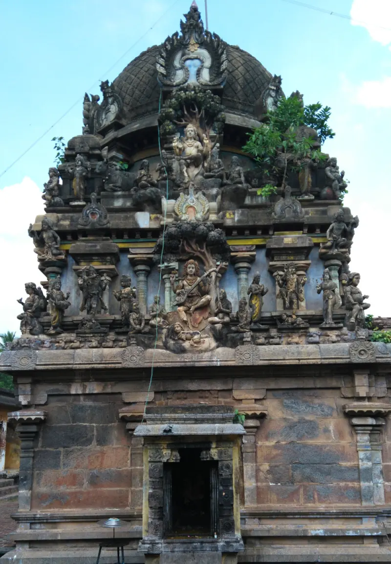 A domed shrine tower decorated with many sculpted figures above a brick and stone wall with a small doorway.