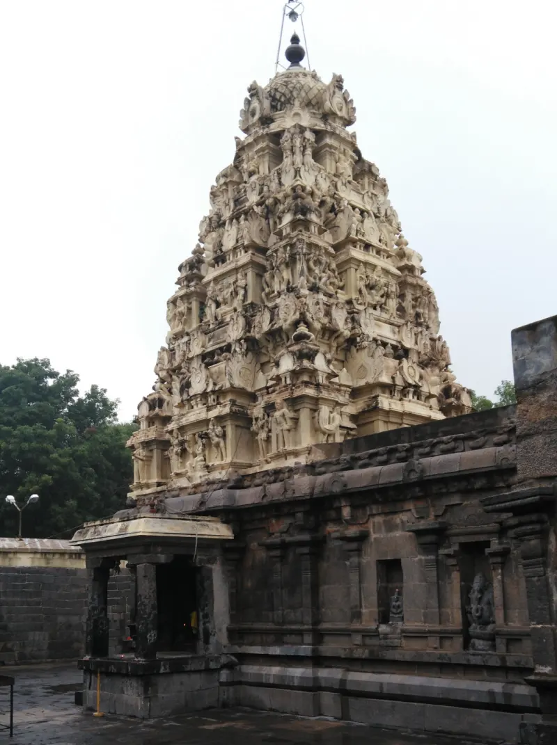 A tall tower of pale carved figures above a dark stone sanctum wall, with a small pillared shrine at the left.
