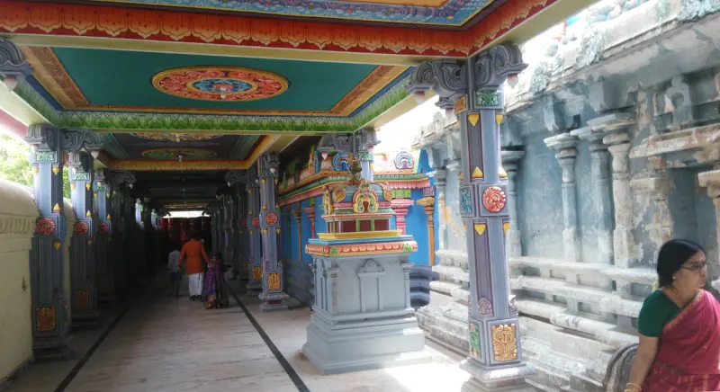 A long painted corridor with pillars, a small shrine in the middle and people walking