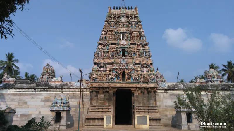 A tall tiered gateway tower covered in painted figures above a stone wall and a dark entrance