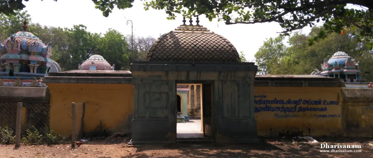 Stone entrance gateway with a lattice dome in a yellow wall, shrine roofs and trees behind