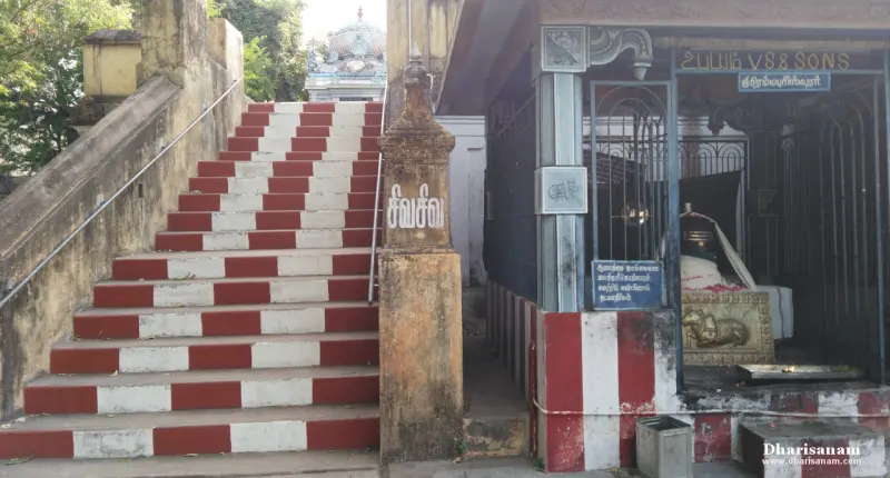 A red-and-white stairway beside a railed shrine with a lingam, a small tower visible beyond