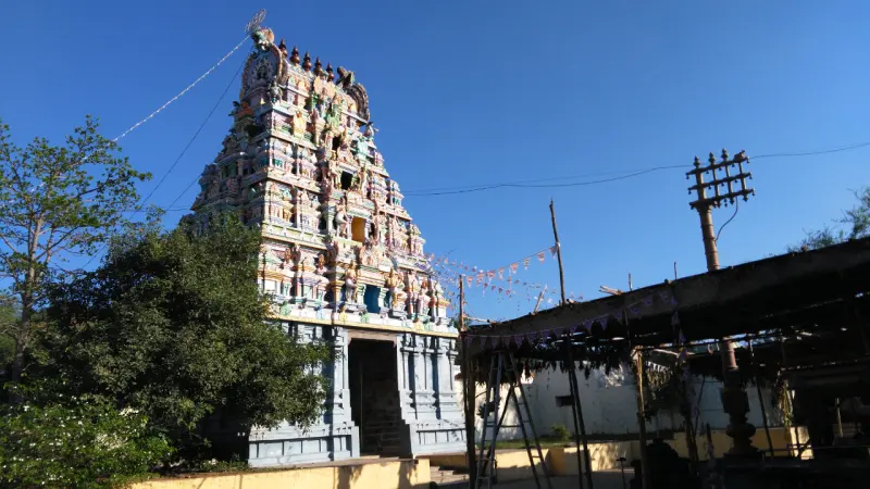 A tall painted tower with many tiers rising above a stone base, with trees on the left and a roofed shed on the right