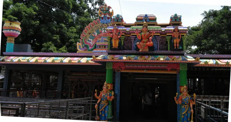 A colourful porch with painted deity figures along its roof and two standing figures on pillars at the front.
