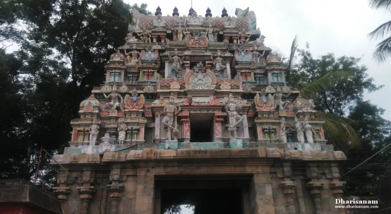 A tiered gopuram with painted stucco figures rising above a dark stone gateway.
