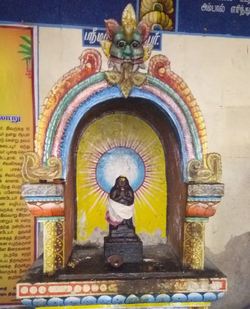 Small dark image in white cloth, seated before a yellow halo, in a niche arched in many colours