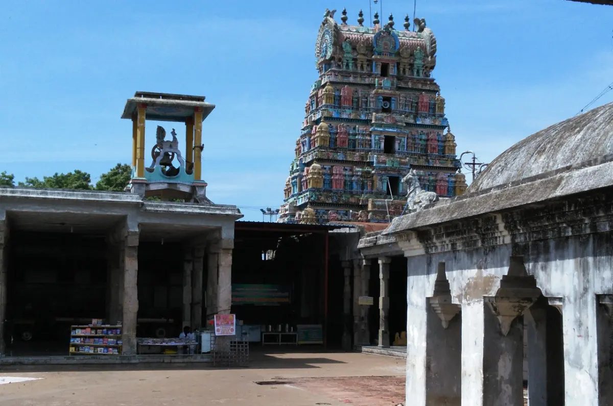 A colourful temple tower rising above a courtyard, with a small pillared canopy and stone corridors in front.