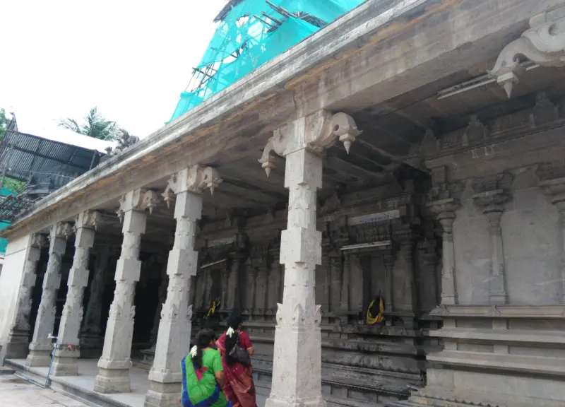 Two women walking along a stone pillared corridor with green netting over the tower above