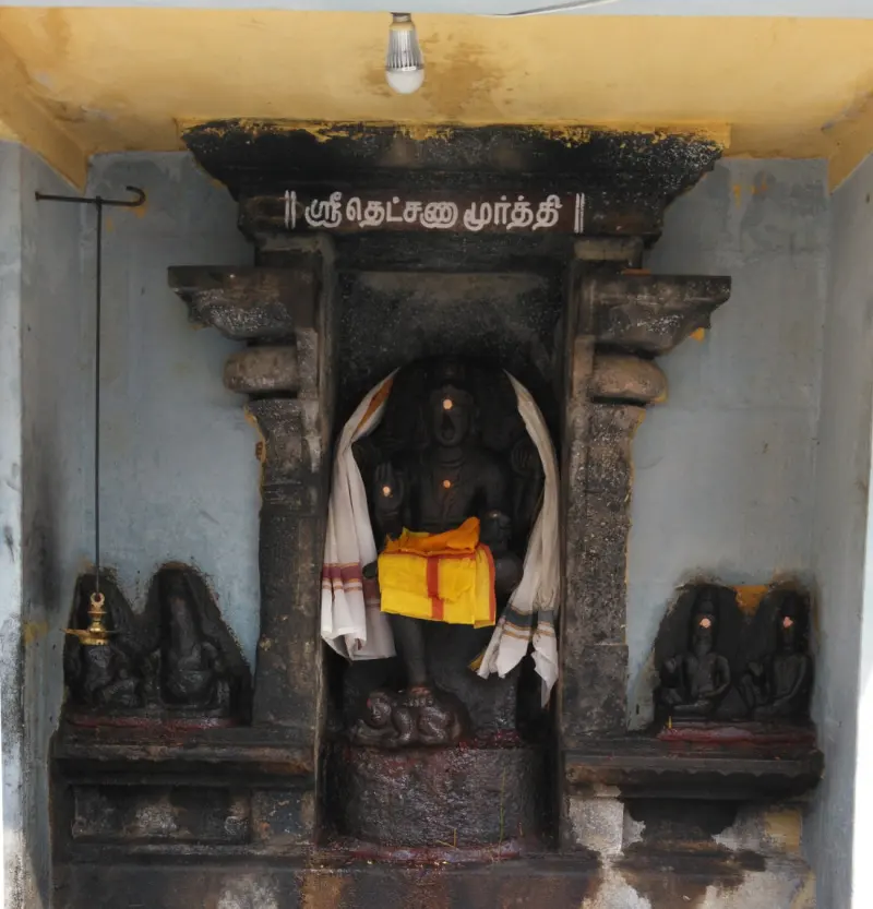 Stone Dakshinamurthy idol with a yellow cloth, flanked by idols