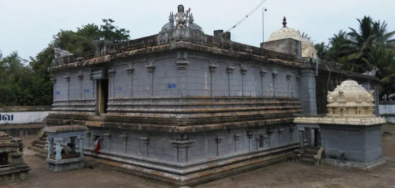 A long grey stone wall with a statue on the roof and a small domed shrine at the right.