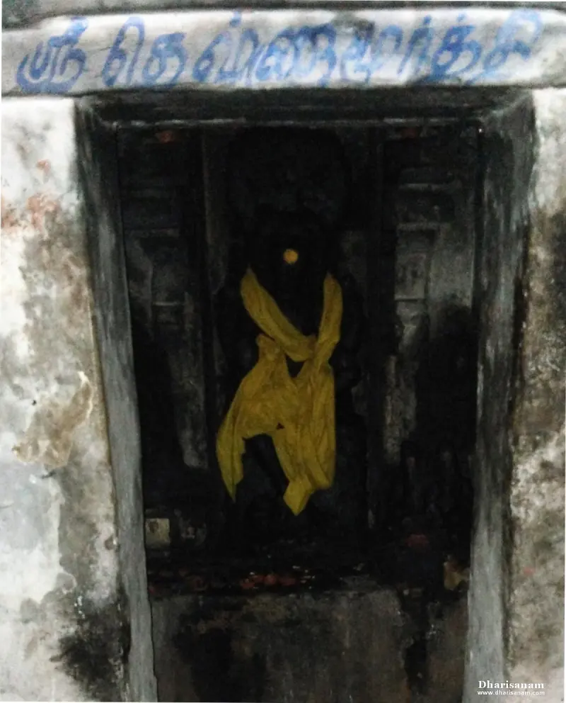 Dark niche with a blue Tamil name board above and an idol covered with a yellow cloth