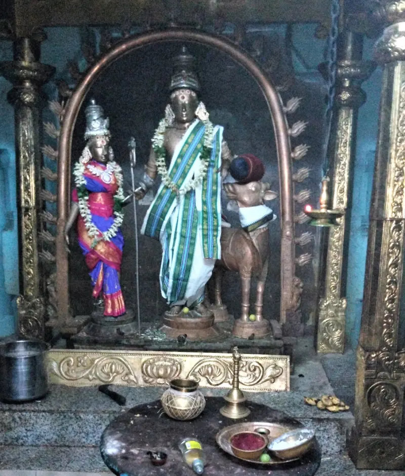 Two garlanded bronze figures stand under a copper arch with a small bull beside them; offerings lie in front.