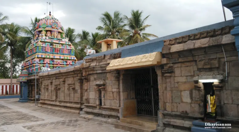 A long stone wall of the corridor with an open gateway, and a colourful tower beyond it