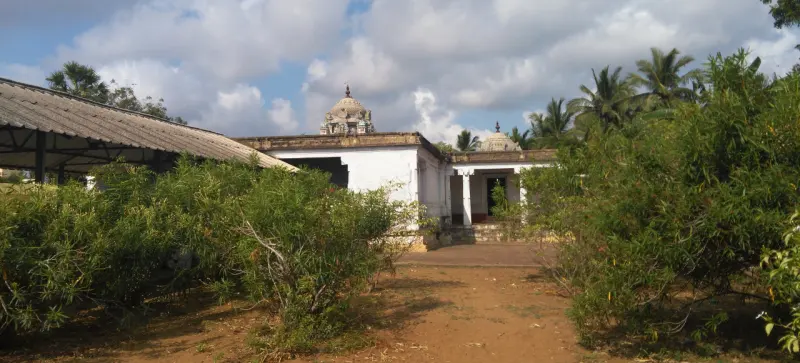 White temple buildings with two small domed towers behind shrubs and a dirt path