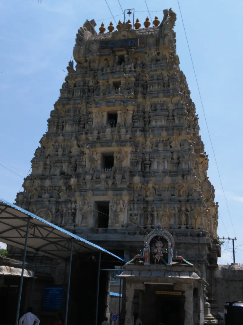 A tall stone gateway tower covered in carved figures, with a small shrine at its foot