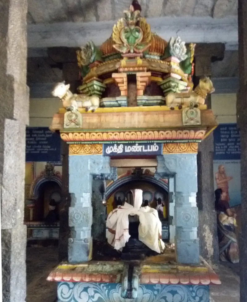 Small stone shrine with bulls on its roof and a lingam in white cloth, under a Tamil name board