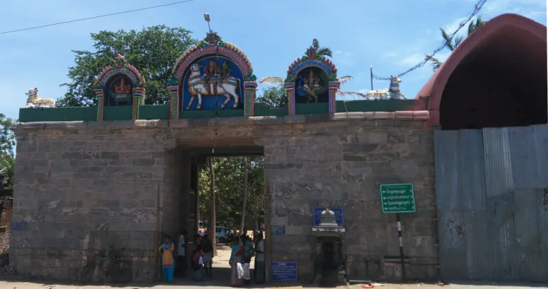 A stone gateway with painted figures on its roof, with people at its entrance and a signboard at right.