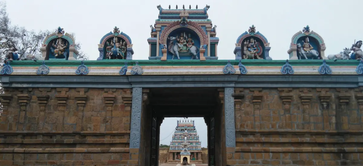 Stone gateway topped with painted figures; a temple tower is seen through the passage