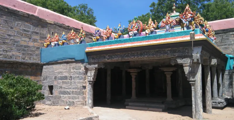 A stone mandapam with a row of colourful figures of deities along the edge of its roof.