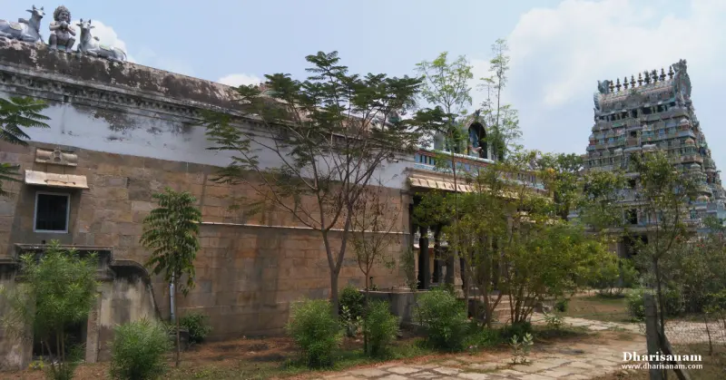 Stone temple wall with trees in front and the gopuram visible at right
