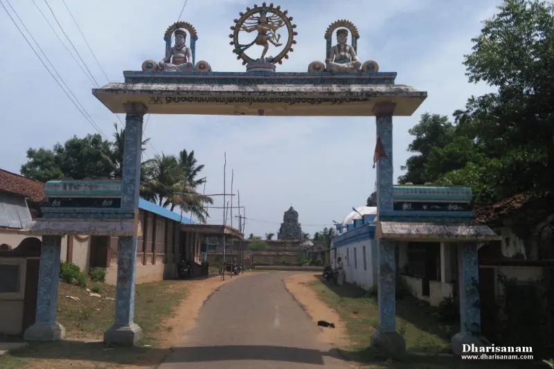 A road passing under an arch topped with a dancing Nataraja figure, a tower in the distance