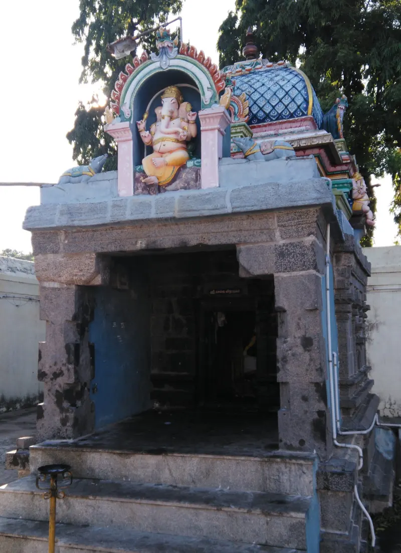 A small grey stone shrine with steps, and a painted seated Ganesha figure in an arch above the doorway