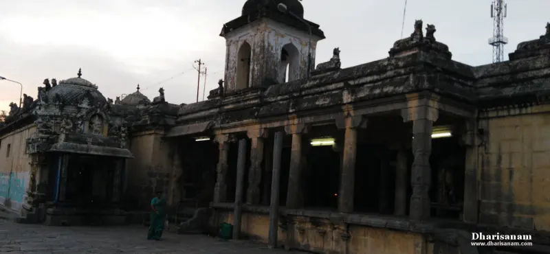 A long stone corridor with pillars and lights, a small carved shrine at the left and a green-clad woman walking
