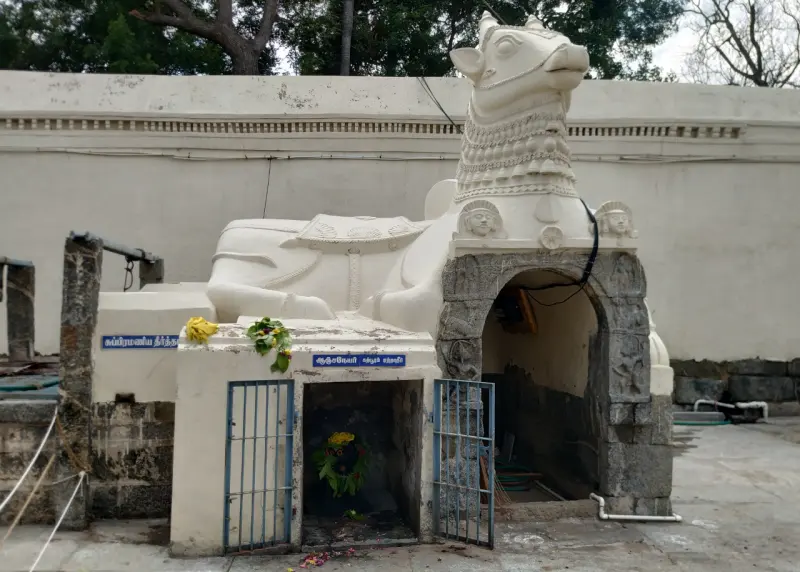 A large white Nandi statue above a small stone shrine with a blue gate, in front of a plain white wall.